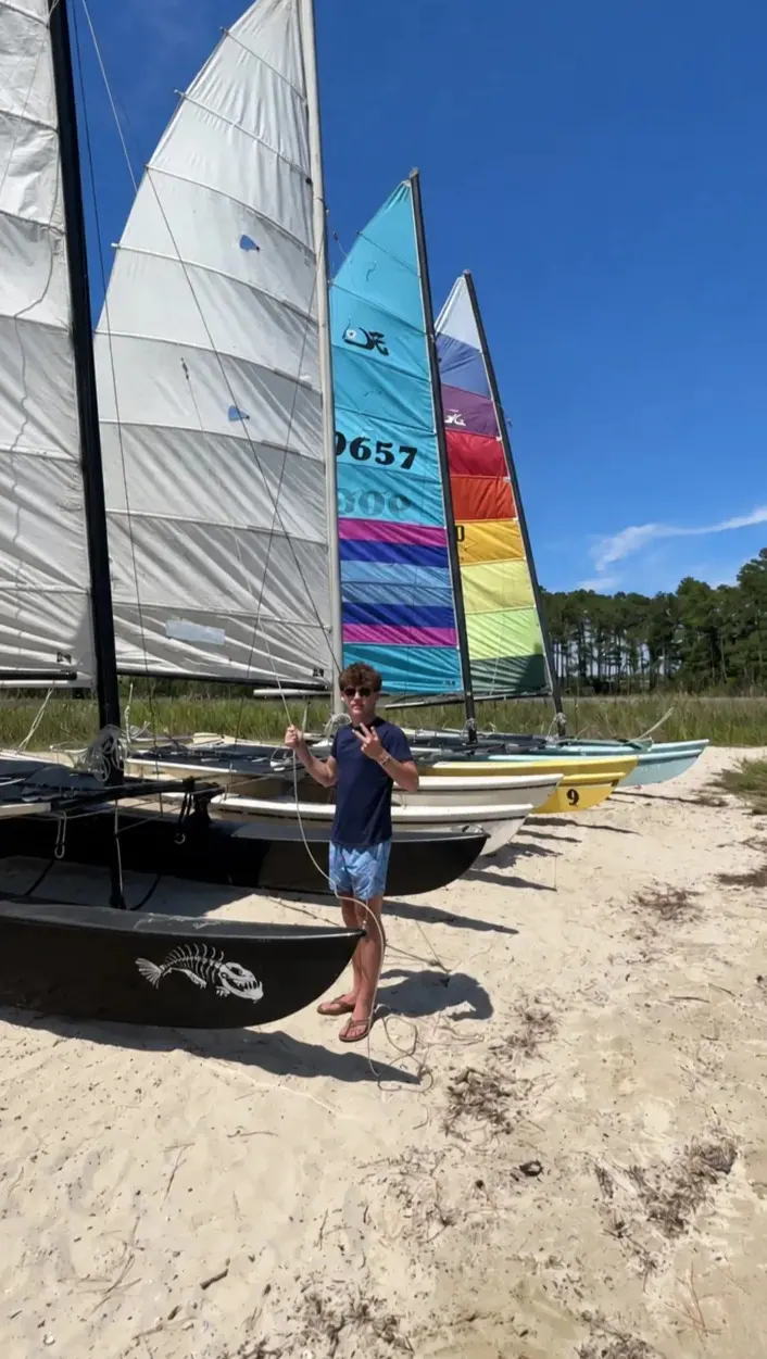 Dylan with a row of Hobie Cats on the beach